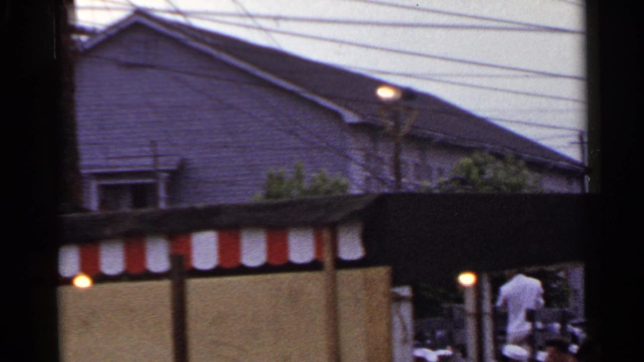 Japan street scene with a red-and-white striped awning, overhead wires, low-rise buildings, and pedestrians moving nearby.
