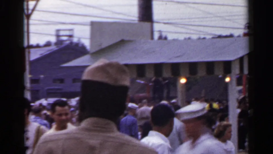 1950s Japan street crowd with men in light shirts and hats moving past a roofed storefront or awning area.