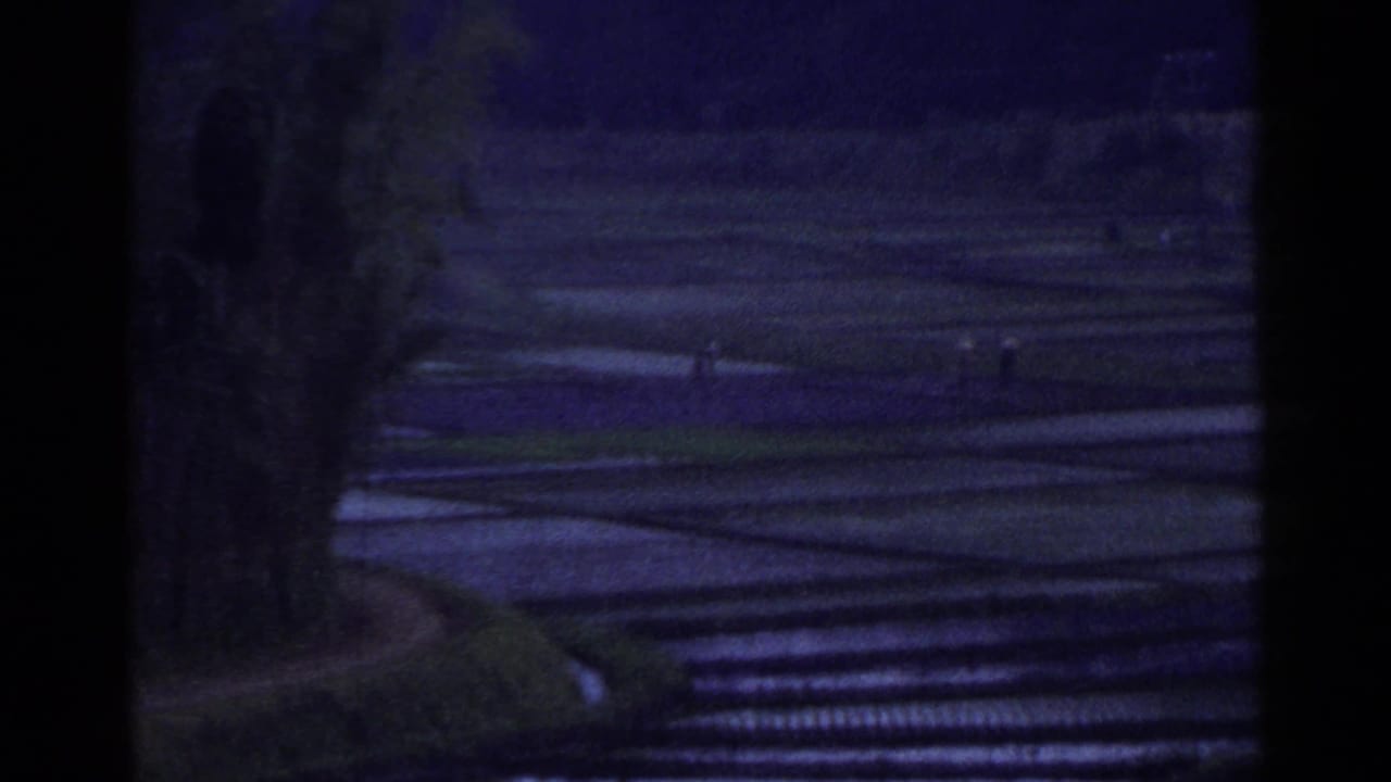Dark view of flooded terraced paddies with small distant figures.
