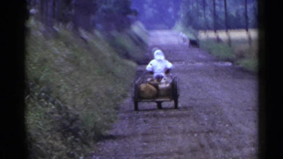 A handcart loaded with harvested bundles is pulled along a rural Japanese dirt road in the 1953 home-movie footage.