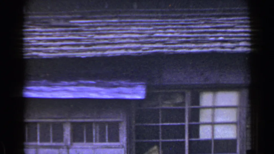 1953 Japan 8mm frame showing lower wooden siding, multi-pane windows, pale curtains or panels, and strong film-edge darkening.