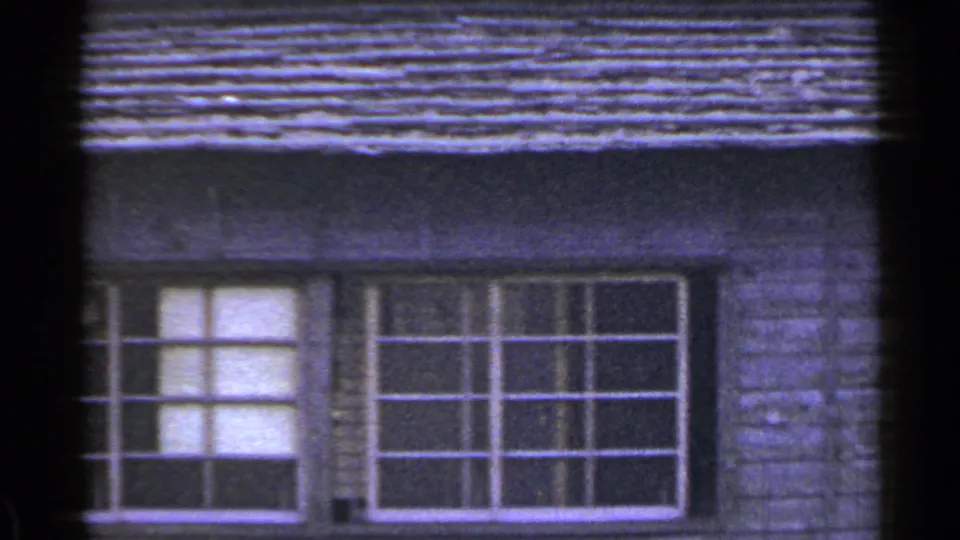 1953 Japan home-movie frame showing two large multi-pane windows set into weathered wooden siding below a low roofline.