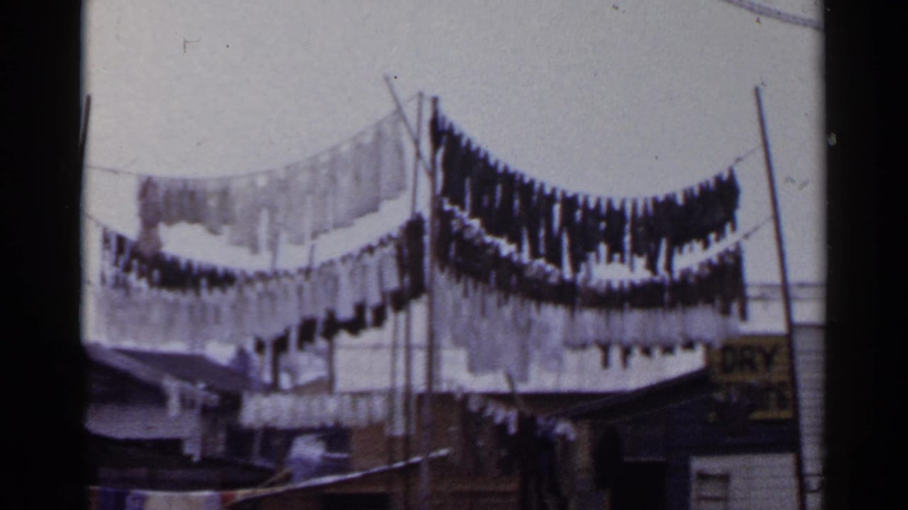 1953 Japan 8mm frame showing laundry hanging on outdoor lines near poles and low buildings.
