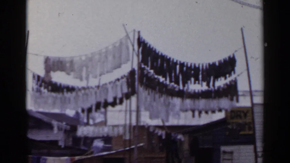 1953 Japan 8mm frame showing laundry hanging on outdoor lines near poles and low buildings.