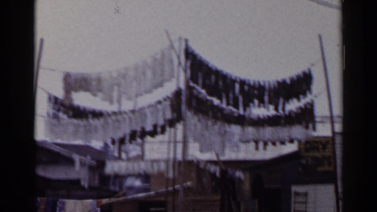 Laundry dries on elevated lines in a 1953 Japan home-movie view with poles, wires, and small structures below.