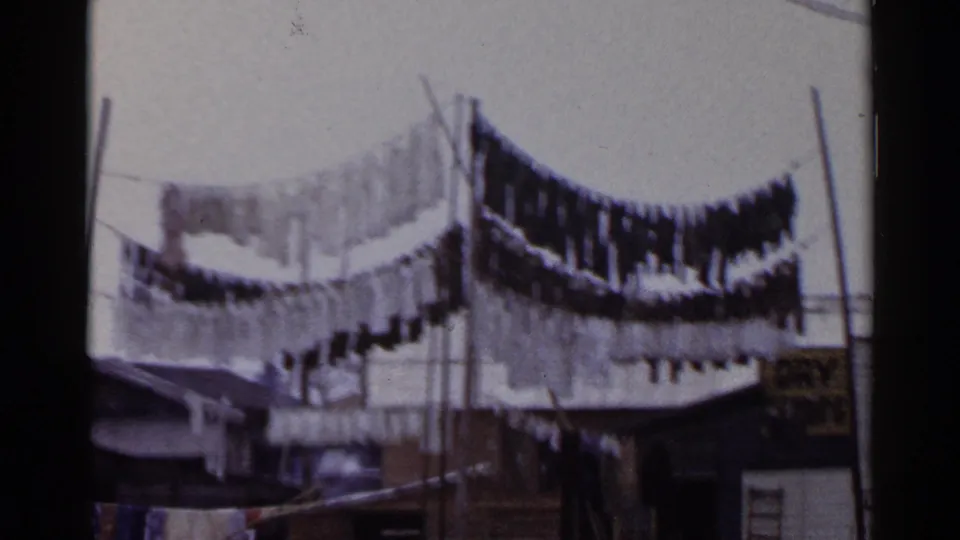 Laundry dries on elevated lines in a 1953 Japan home-movie view with poles, wires, and small structures below.