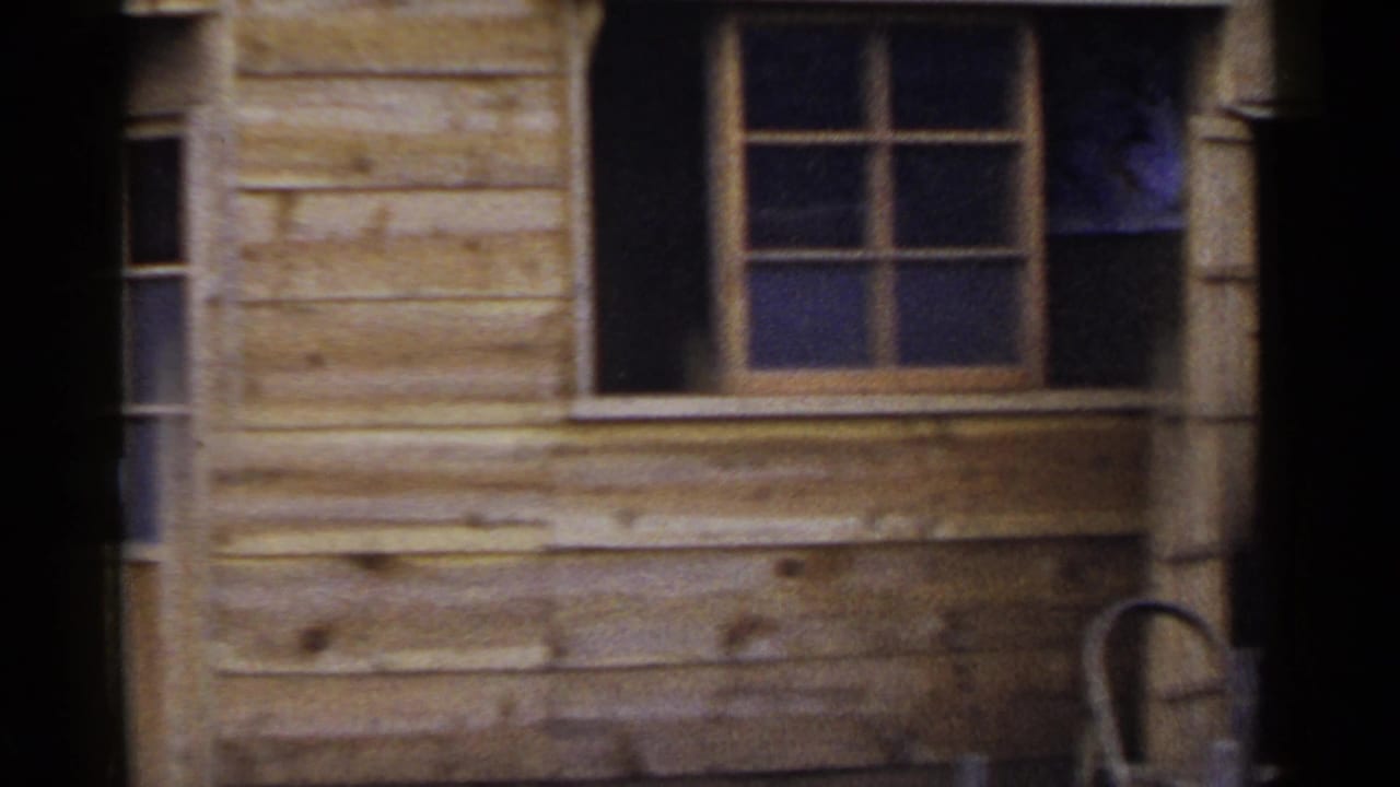 Wooden cabin exterior with small windows, dark doorway, chair, and plank siding.