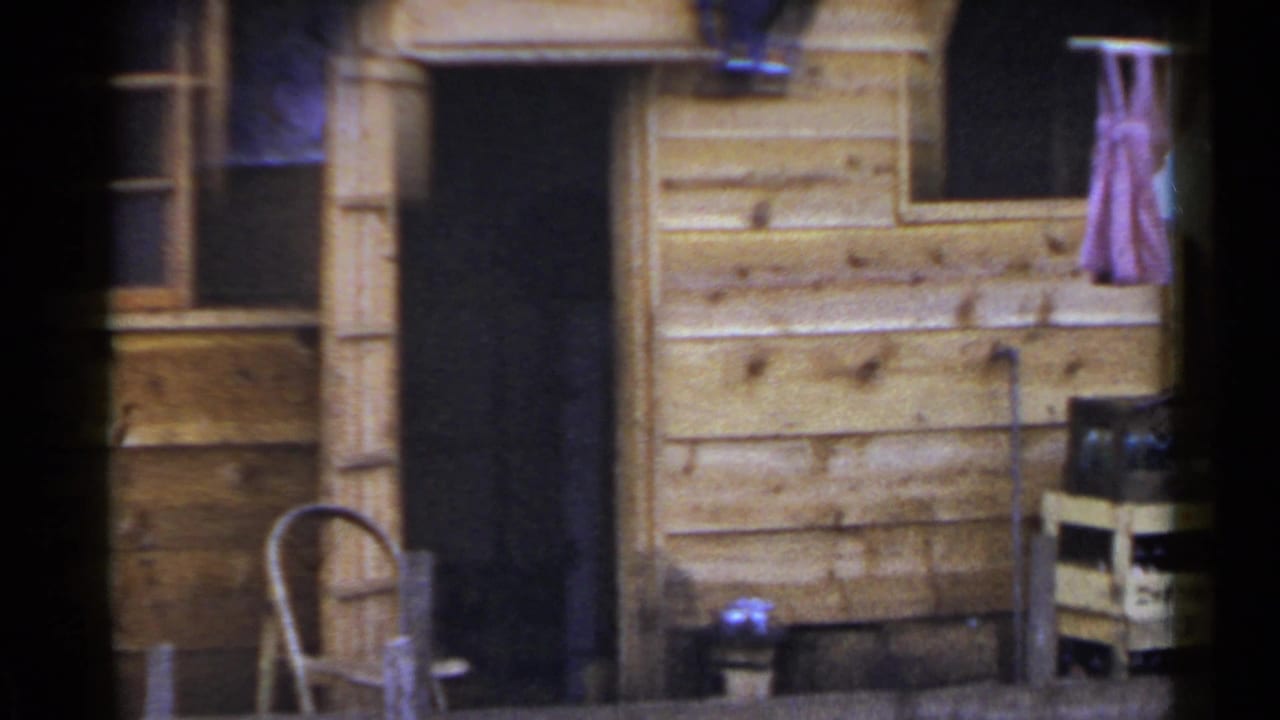 Cabin doorway and wall with a chair, crate, bucket, and laundry hanging at the side.