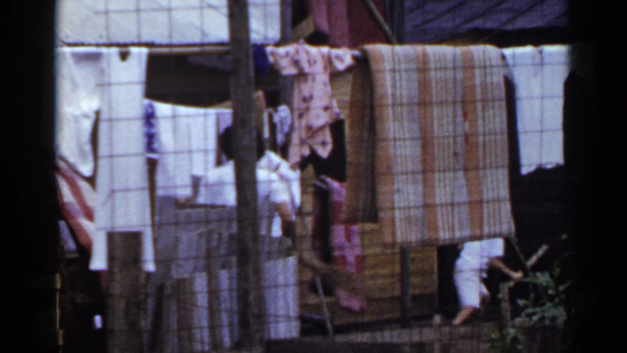 1953 Japan exterior frame with shirts and blankets on a line, a woman partly visible, and a small figure near the edge of the yard.
