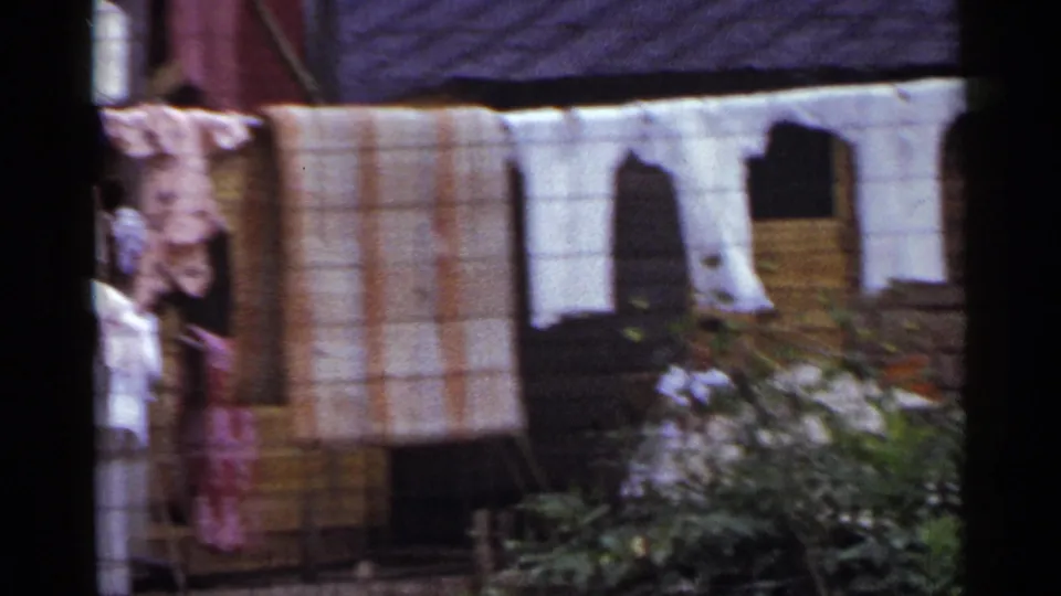 1953 Japan frame with striped blankets, white garments, a wooden exterior, and garden foliage partially covering the lower view.