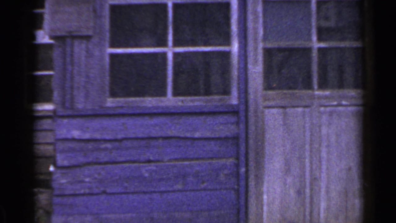 1953 Japan home-movie frame showing a purple-toned wooden wall, small-paned windows, and a close view of a weathered doorway.
