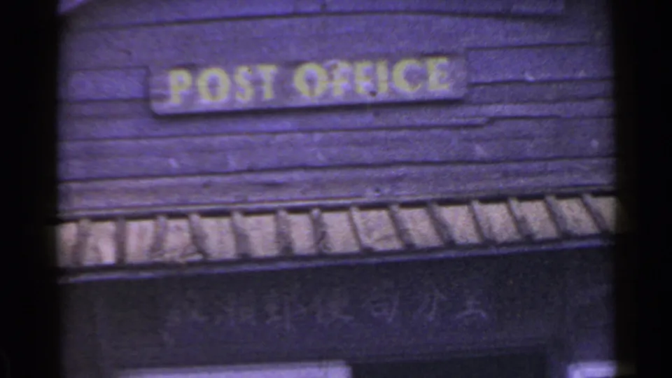 1953 Japan 8mm frame showing the POST OFFICE sign, red mailbox, door, window, and faint Japanese lettering on the wooden facade.