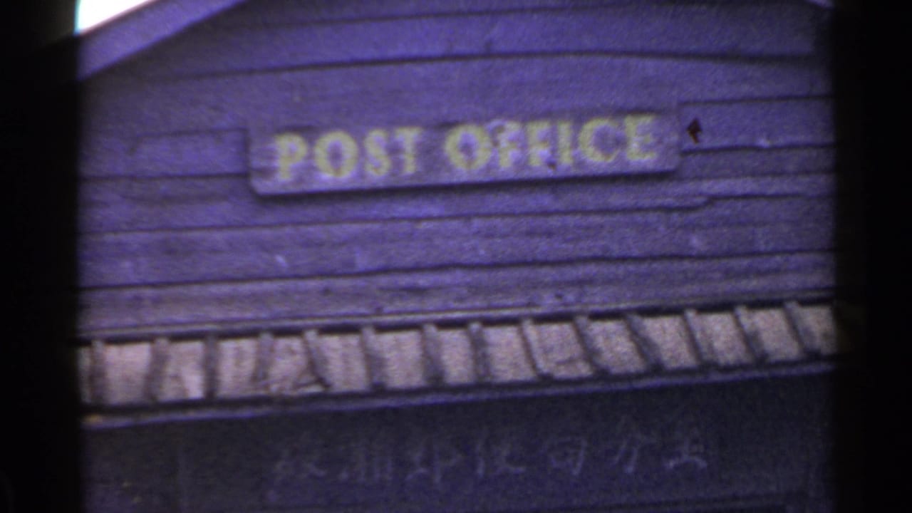A faded 8mm view of the yellow POST OFFICE sign on a weathered wooden building in Japan.