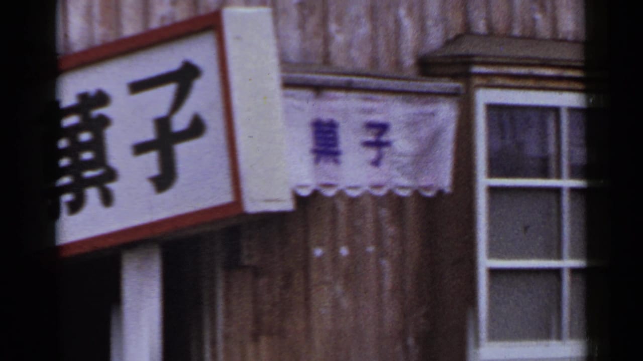 1953 Japan storefront detail with Japanese characters, a small cloth banner, wood siding, and a white-framed window.