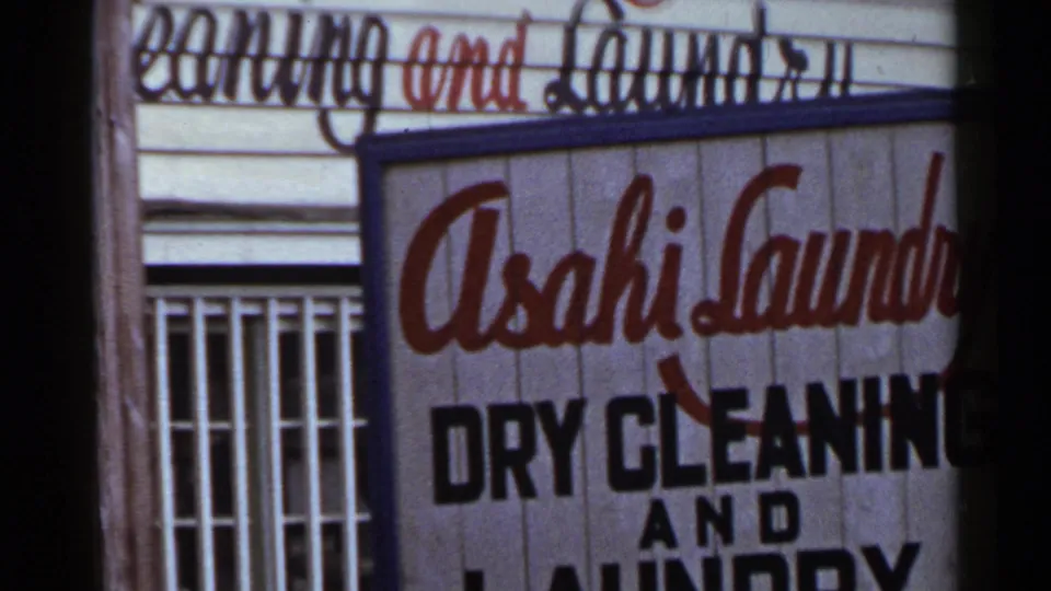 1953 Japan storefront with prominent Asahi Laundry Dry Cleaning and Laundry sign, barred windows, and weathered wood siding.