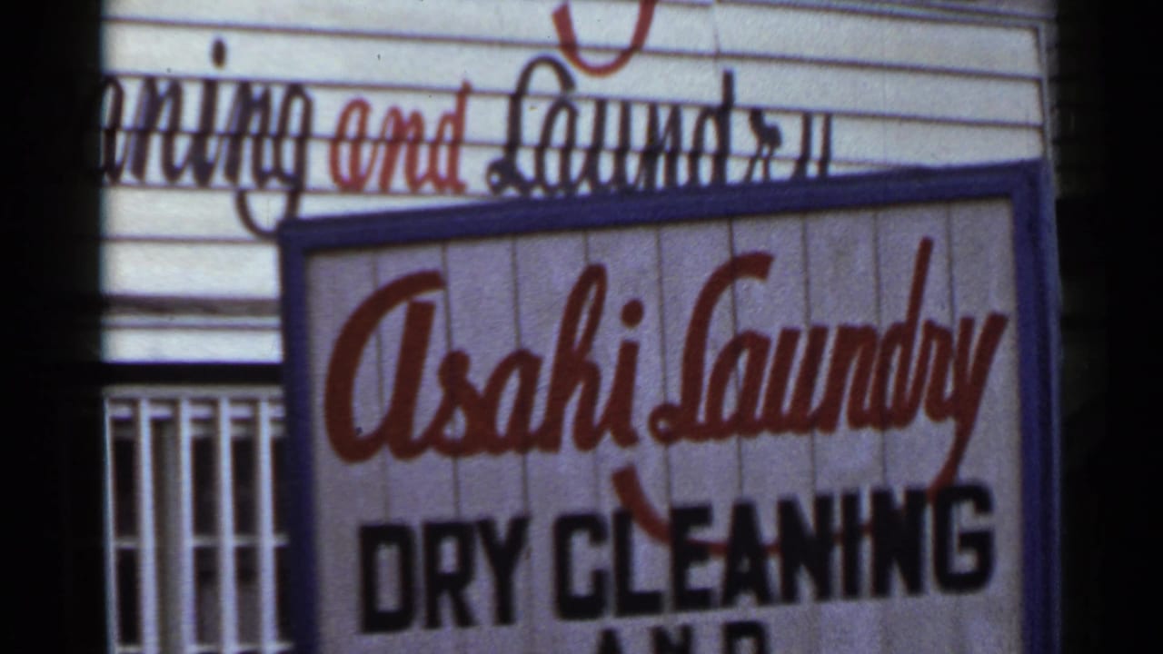 1953 Japan 8mm frame showing a close-up of the Asahi Laundry dry cleaning sign with red script lettering above black text.