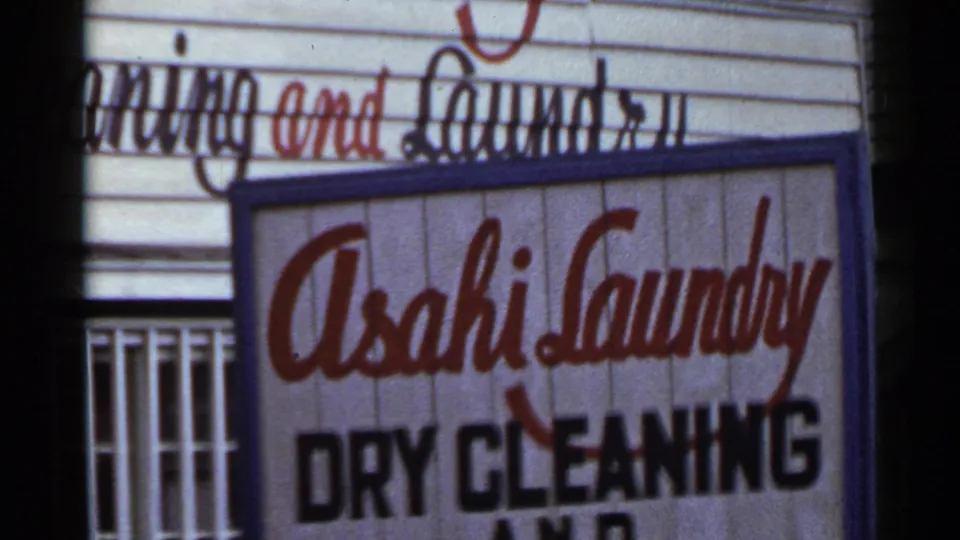 1953 Japan 8mm frame showing a close-up of the Asahi Laundry dry cleaning sign with red script lettering above black text.