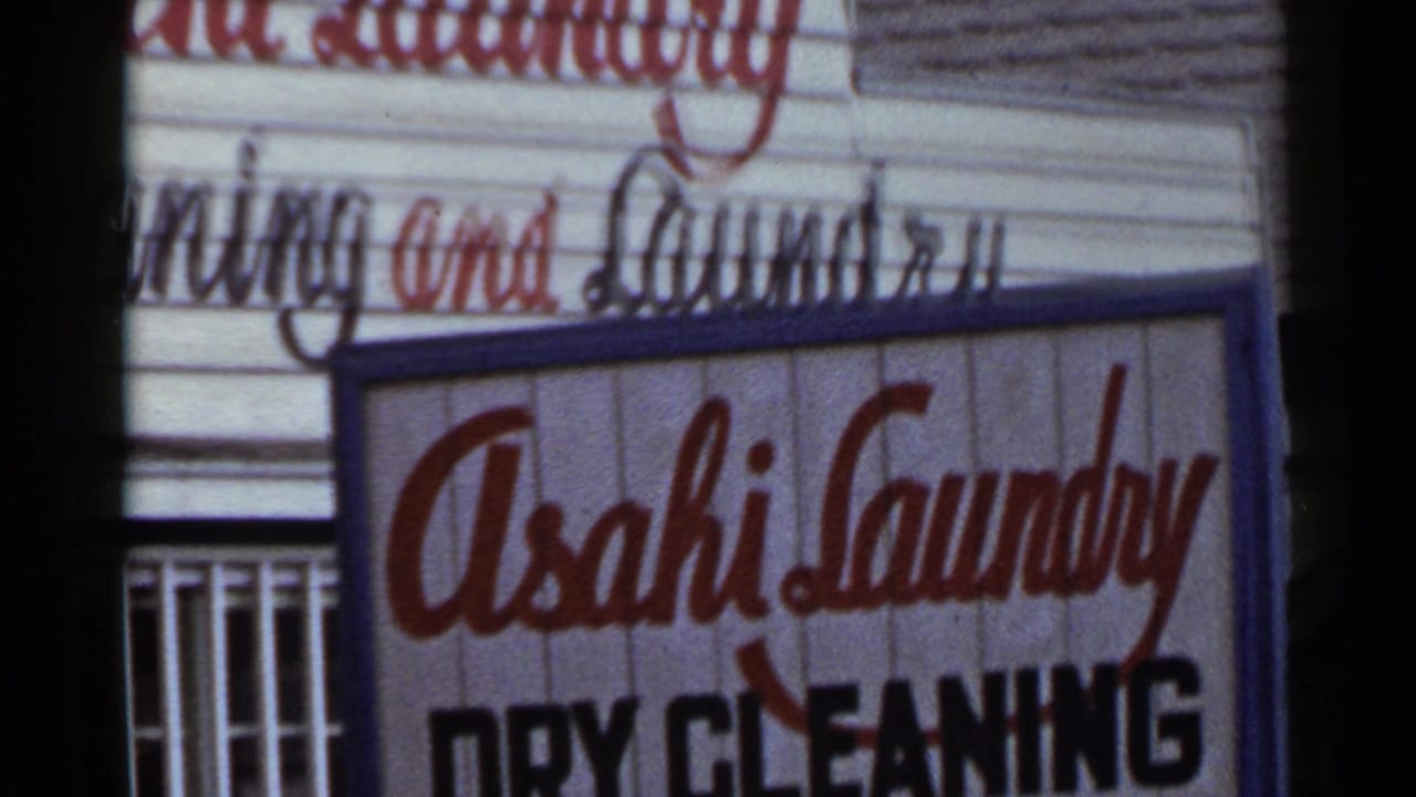 1953 Japan frame with the Asahi Laundry sign slightly shifted, showing the red name, black dry cleaning text, and building facade.