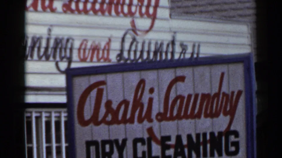 1953 Japan frame with the Asahi Laundry sign slightly shifted, showing the red name, black dry cleaning text, and building facade.