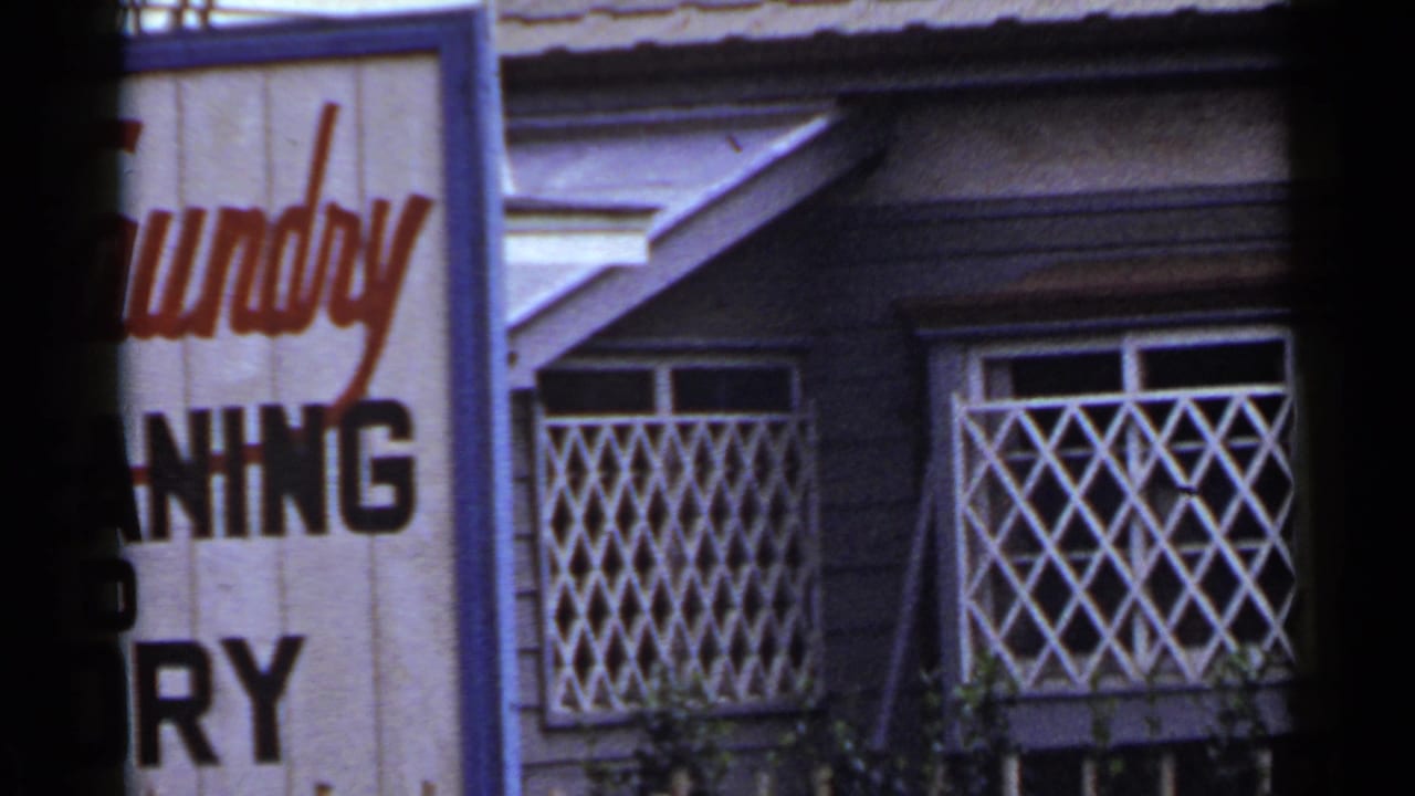 1953 Japan frame with the sign moving partly out of view, revealing more facade, blue trim, and diamond-patterned window grilles.
