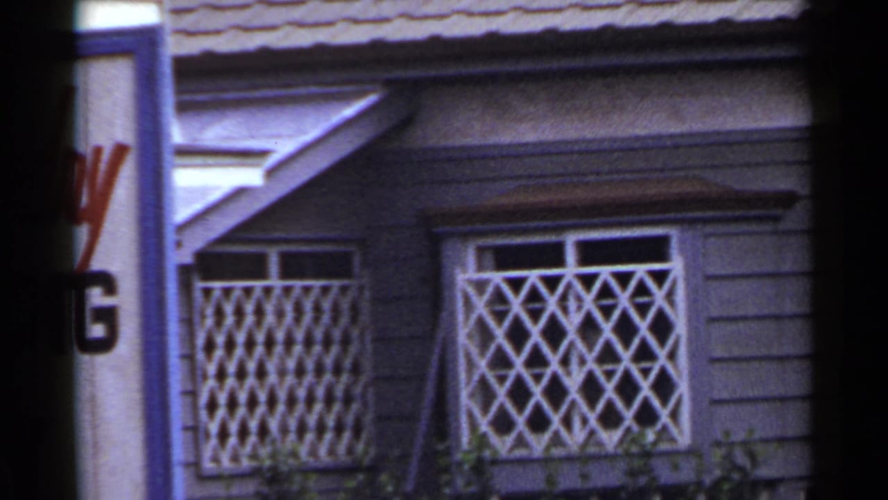 1953 Japan 8mm frame showing a purple-sided storefront with white lattice window guards, tiled roof edge, and partial signage.