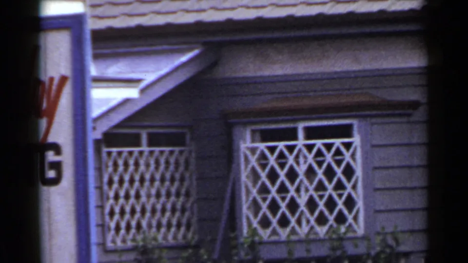 1953 Japan 8mm frame showing a purple-sided storefront with white lattice window guards, tiled roof edge, and partial signage.