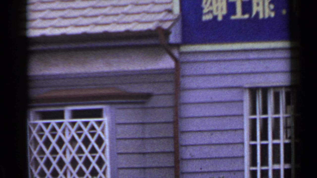 1953 Japan frame showing the upper shop facade, white lattice window guards, and a cropped blue sign with Japanese text.