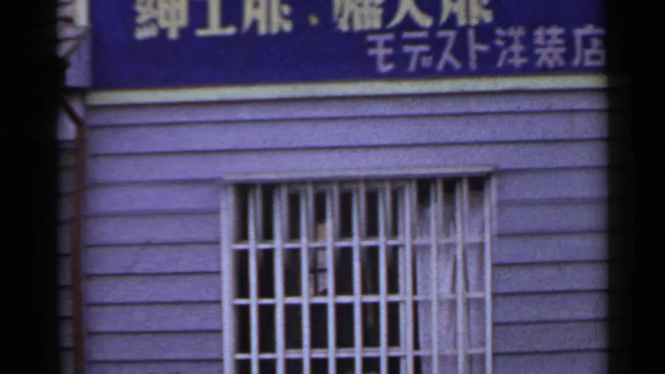 1953 Japan 8mm frame showing a blue shop sign with Japanese characters over a barred window and purple exterior siding.