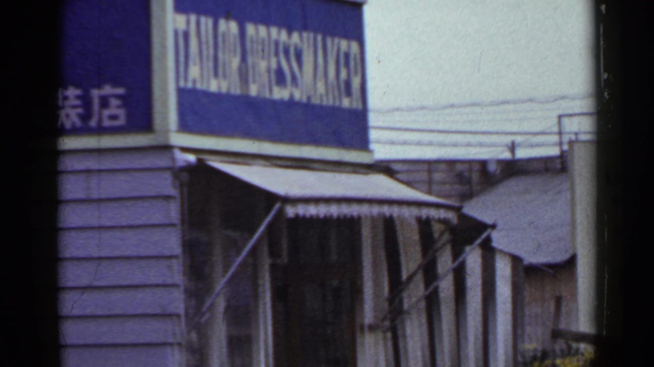 A 1953 Japan street frame centers a blue tailor and dressmaker sign, Japanese characters, awning, and overhead wires.