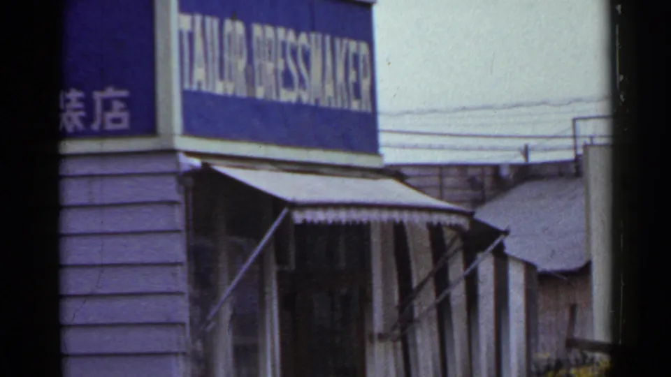 A 1953 Japan street frame centers a blue tailor and dressmaker sign, Japanese characters, awning, and overhead wires.