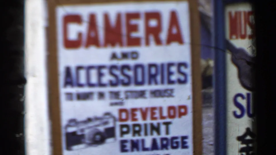 1953 Japan 8mm frame showing a storefront sign advertising camera accessories and photo developing services.