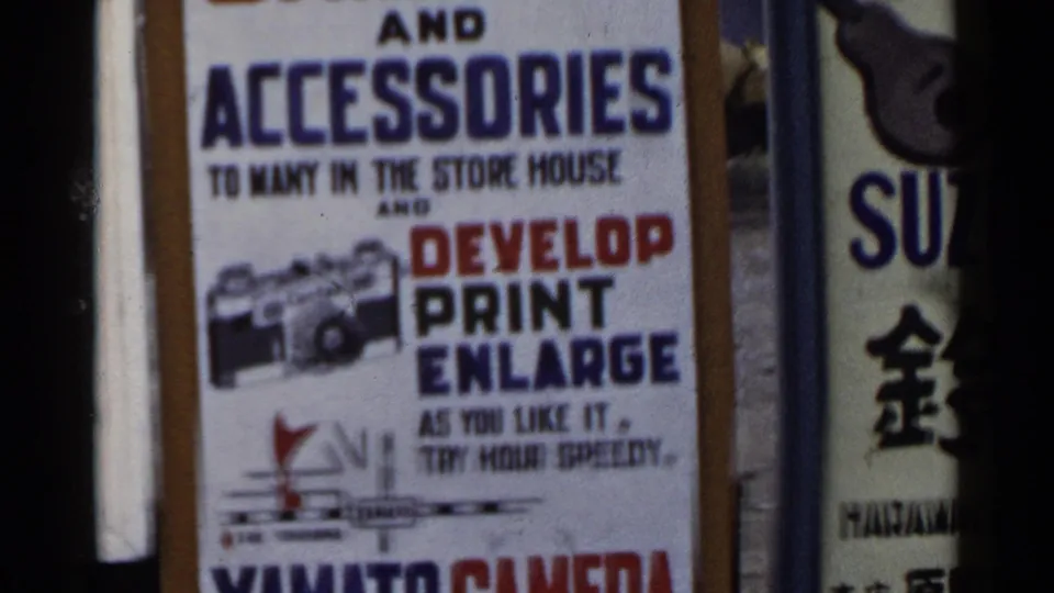 1953 Japan 8mm frame showing the camera accessories sign and adjacent vertical signage, with the advertisement cropped by handheld movement.