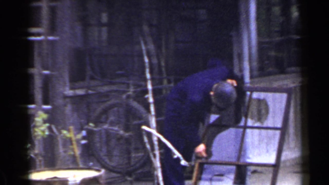 A man in a dark blue jacket and cap bends over a detached window frame outside a weathered building in Japan, 1953.