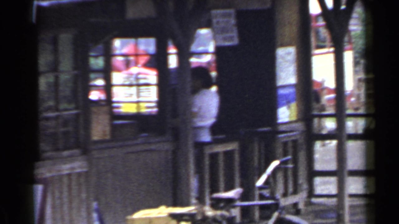 Wooden storefront with windows, posts, a bicycle, and a person standing near an entrance.