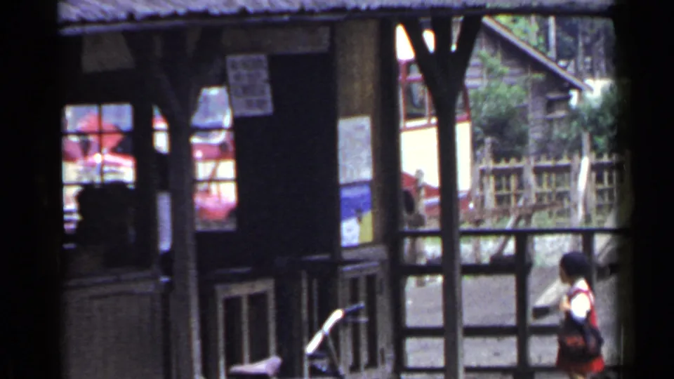 1953 Japan home-movie view of a wooden building corner, windowed facade, bicycle parts, and a person moving through the edge of the frame.