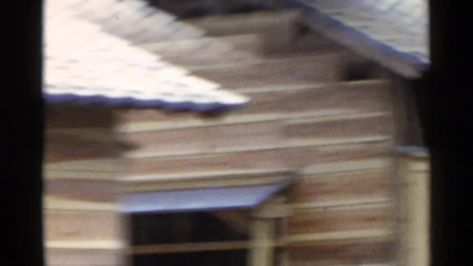 1953 Japan 8mm frame showing layered roof surfaces and wooden walls in a rural Japanese setting.