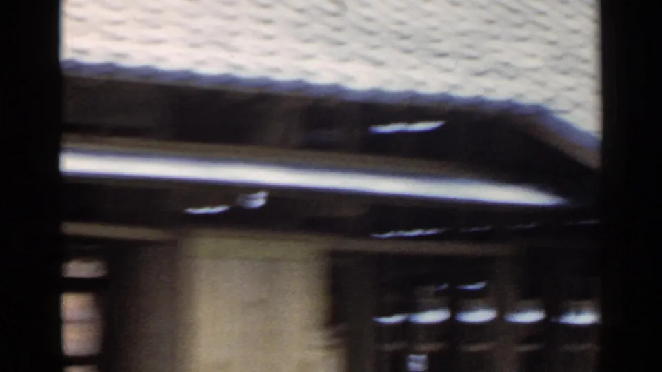 1953 Japan home-movie frame showing a soft, blurred view of a tiled roof, wall, and dark wooden structural elements.