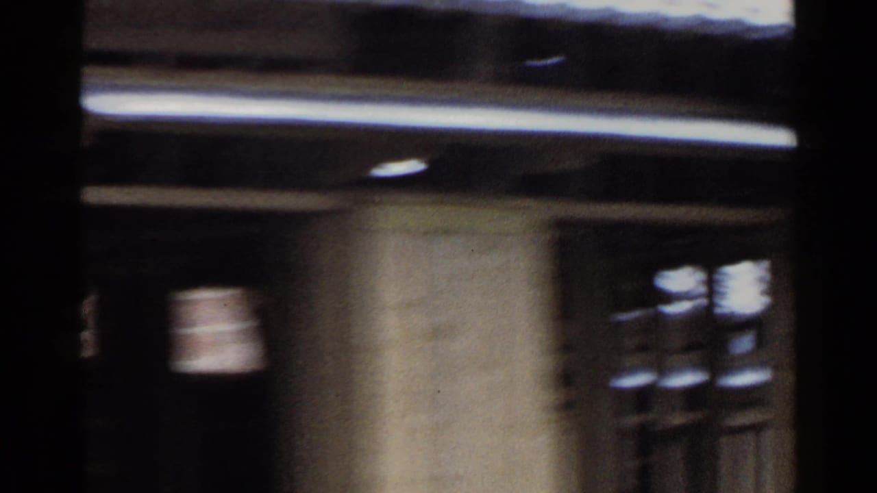 1953 Japan frame with a tiled roof, vertical supports, and dark window or doorway openings captured from a moving camera.