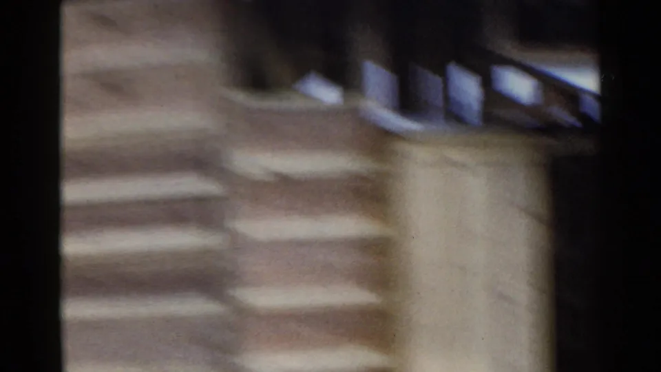 Motion-blurred 1953 Japan home-movie frame showing an exterior wall, possible steps or walkway edges, and wooden structural lines.