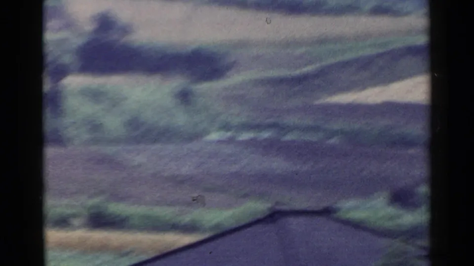Soft 8mm view of Japanese hillside farmland with a dark roofline crossing the lower edge of the frame.