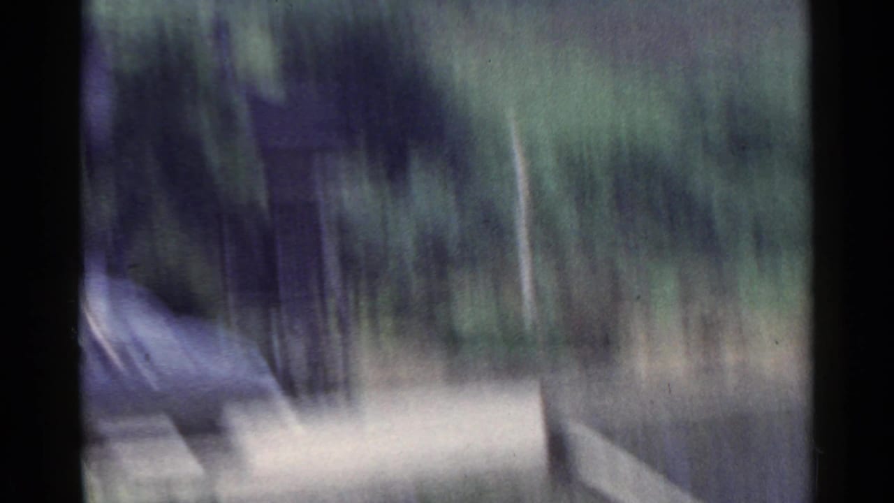 1953 Japan 8mm frame showing blurred roadside trees, a pale road band, and dark film borders from a moving vehicle.