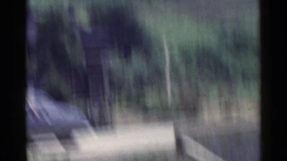 1953 Japan 8mm frame showing blurred roadside trees, a pale road band, and dark film borders from a moving vehicle.