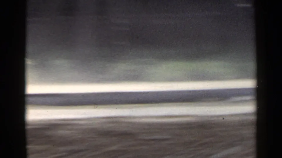 1953 Japan 8mm frame showing a pale road edge, dark foreground band, and green roadside blur from a moving vehicle.