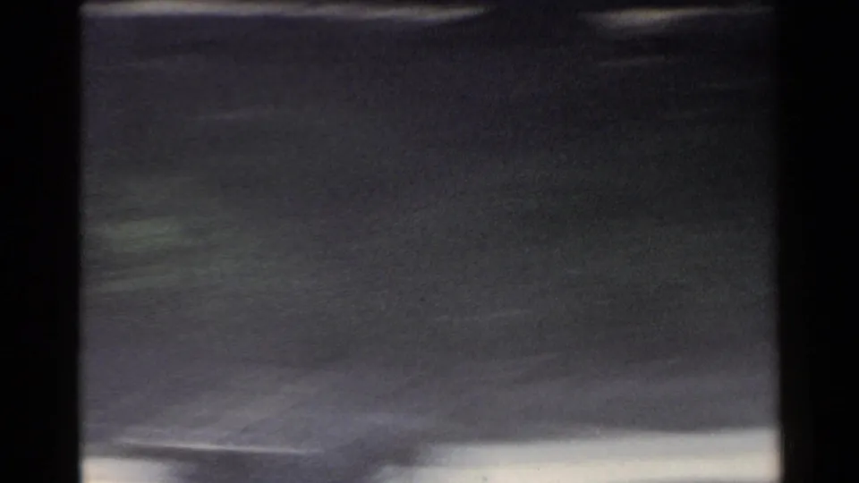 1953 Japan 8mm frame with dark vehicle framing, pale road edge, and blurred roadside scenery passing at speed.