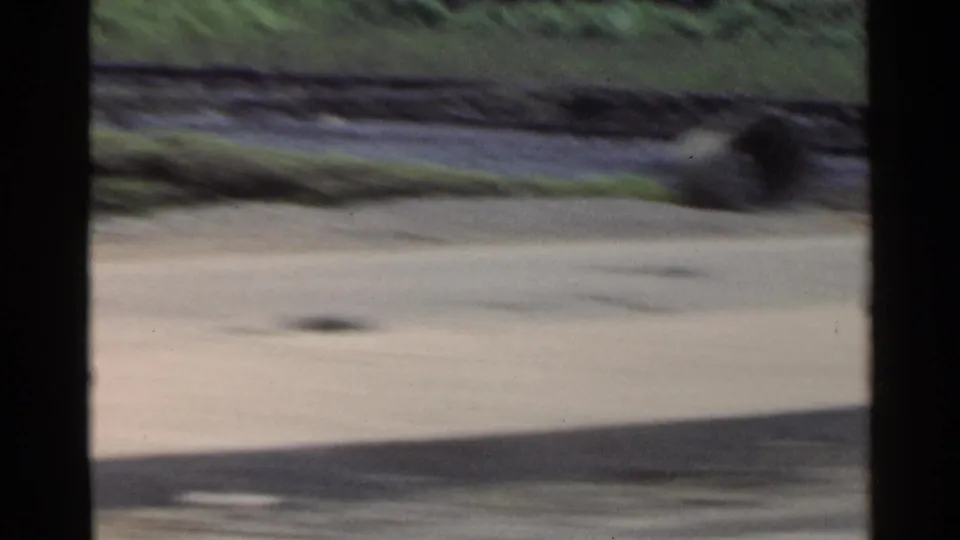 Blurred 1953 Japan home-movie frame looking past a roadside area, greenery, and dark film-edge obstruction from a moving viewpoint.