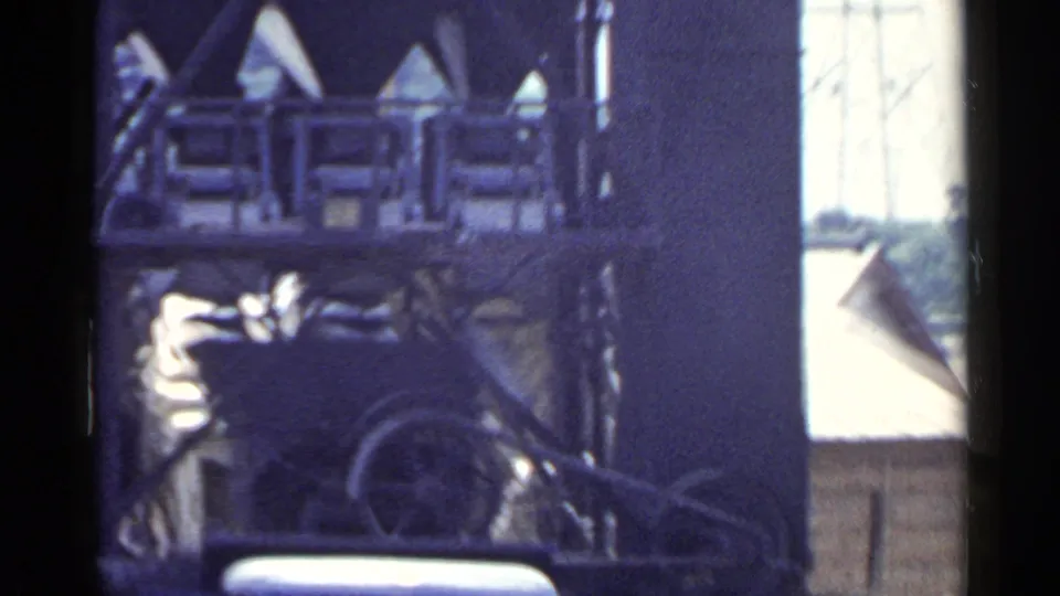 1953 Japan frame of a factory-like building with Japanese characters, timber stacks, and a vehicle partly obscured by shadows.