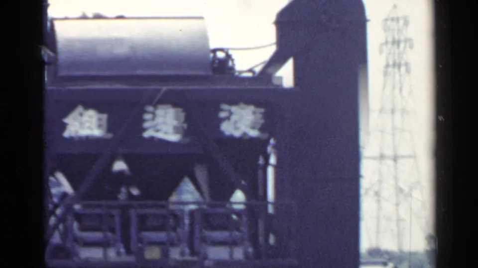 1953 Japan industrial scene showing a tall steel structure with Japanese characters and machinery details in soft 8mm color.