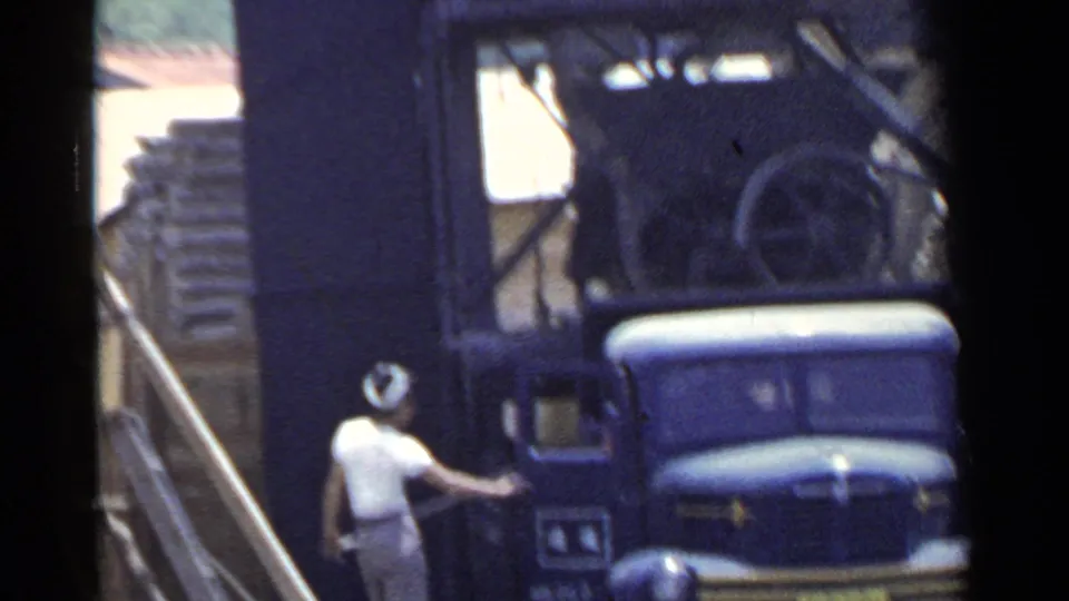 Worker near a blue truck and heavy machinery in a Japanese industrial yard, captured on 1953 8mm home-movie film.