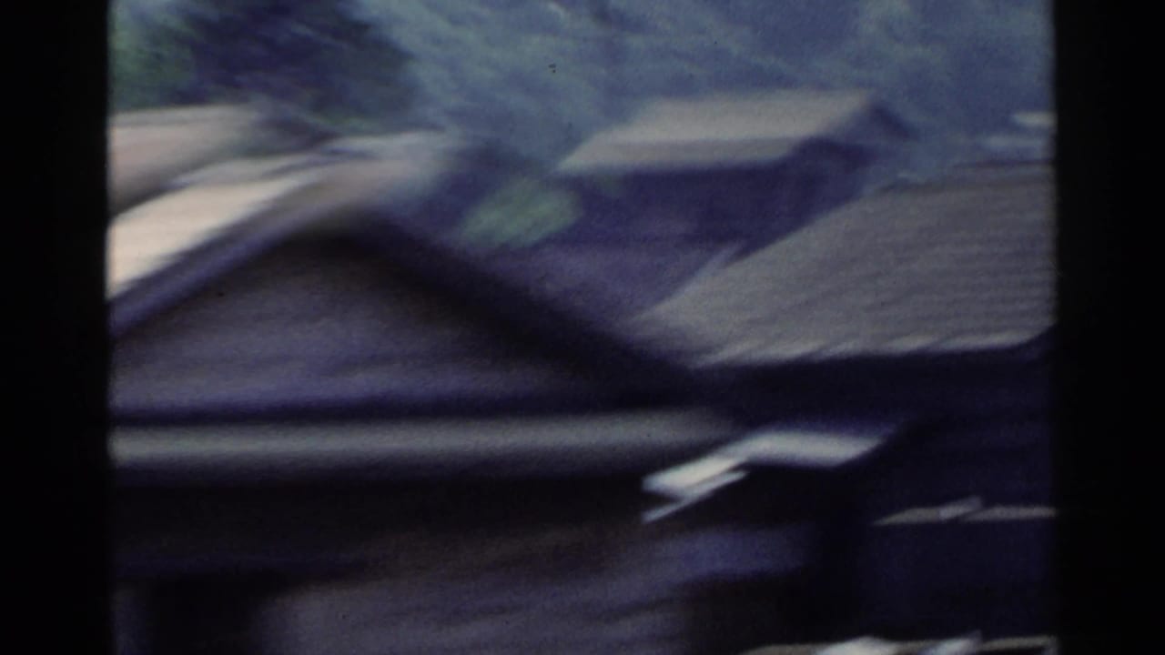 Blurred dark-edged view of rooftops and structures from a moving vehicle.