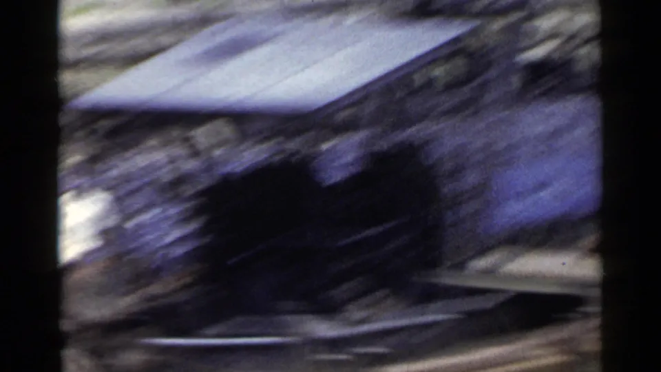 1953 Japan home-movie frame with rooftops, dark foreground shapes, and streaked rail or road edges seen from a moving vehicle.